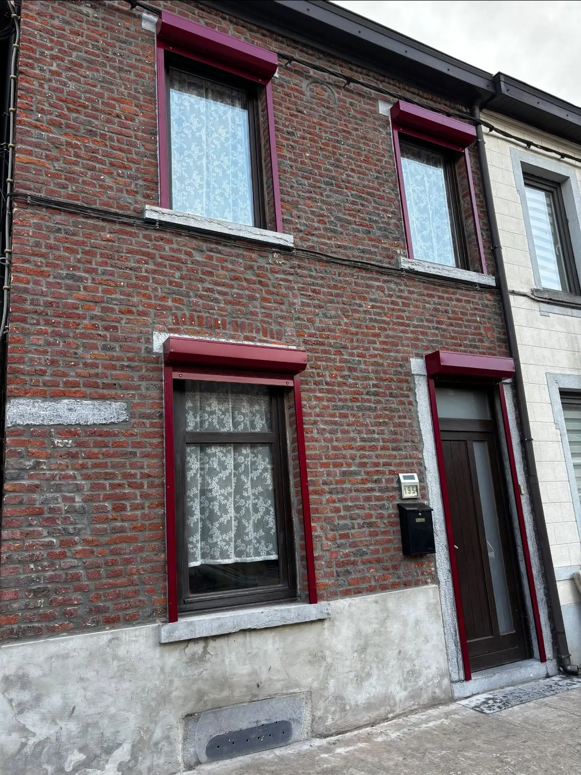 Façade en briques rouges équipée de volets roulants bordeaux aux fenêtres et à la porte d’entrée